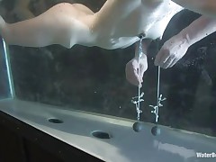 Isobel Wren is in the large fish tank, having her nipples stretched. Her master has nipp clamps with strings attached to weights, having her stay afloat. He fingers her some then removes the weights and has her on her knees, hands behind her back, using a vibrator on her pussy. She's loving it!